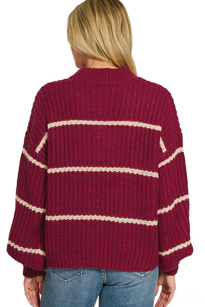 A woman posing in a cabernet red oversized sweater with beige stripes.
