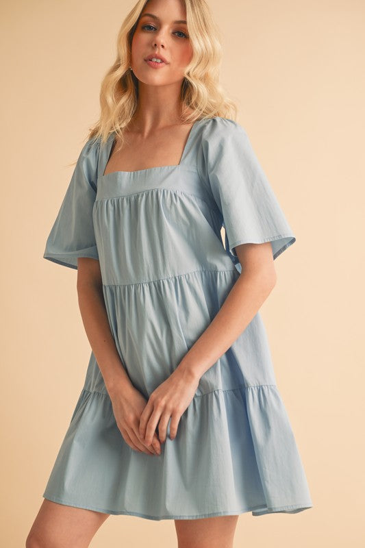 A woman posing in a light blue square neck half sleeve tiered dress.