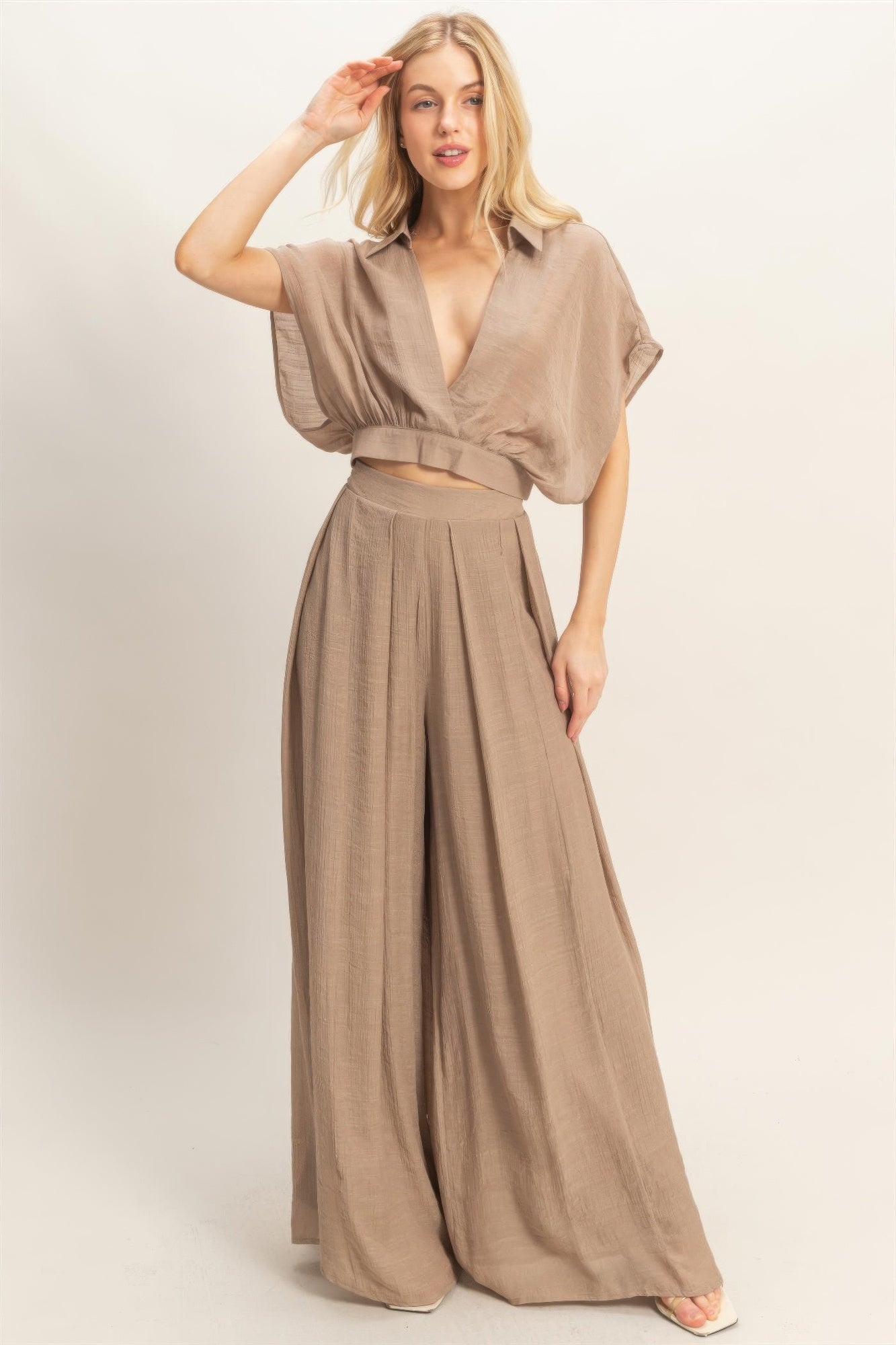 A woman posing in a light mocha-colored collar wrap top & wide-leg pants set.