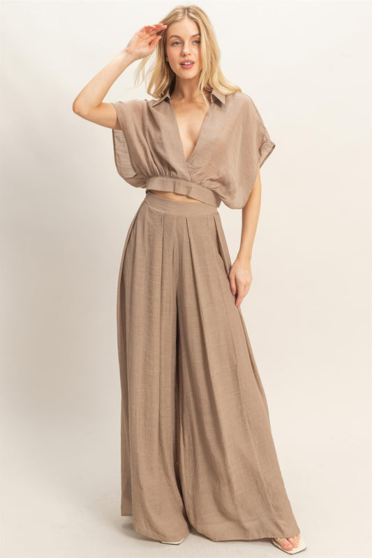 A woman posing in a light mocha-colored collar wrap top & wide-leg pants set.