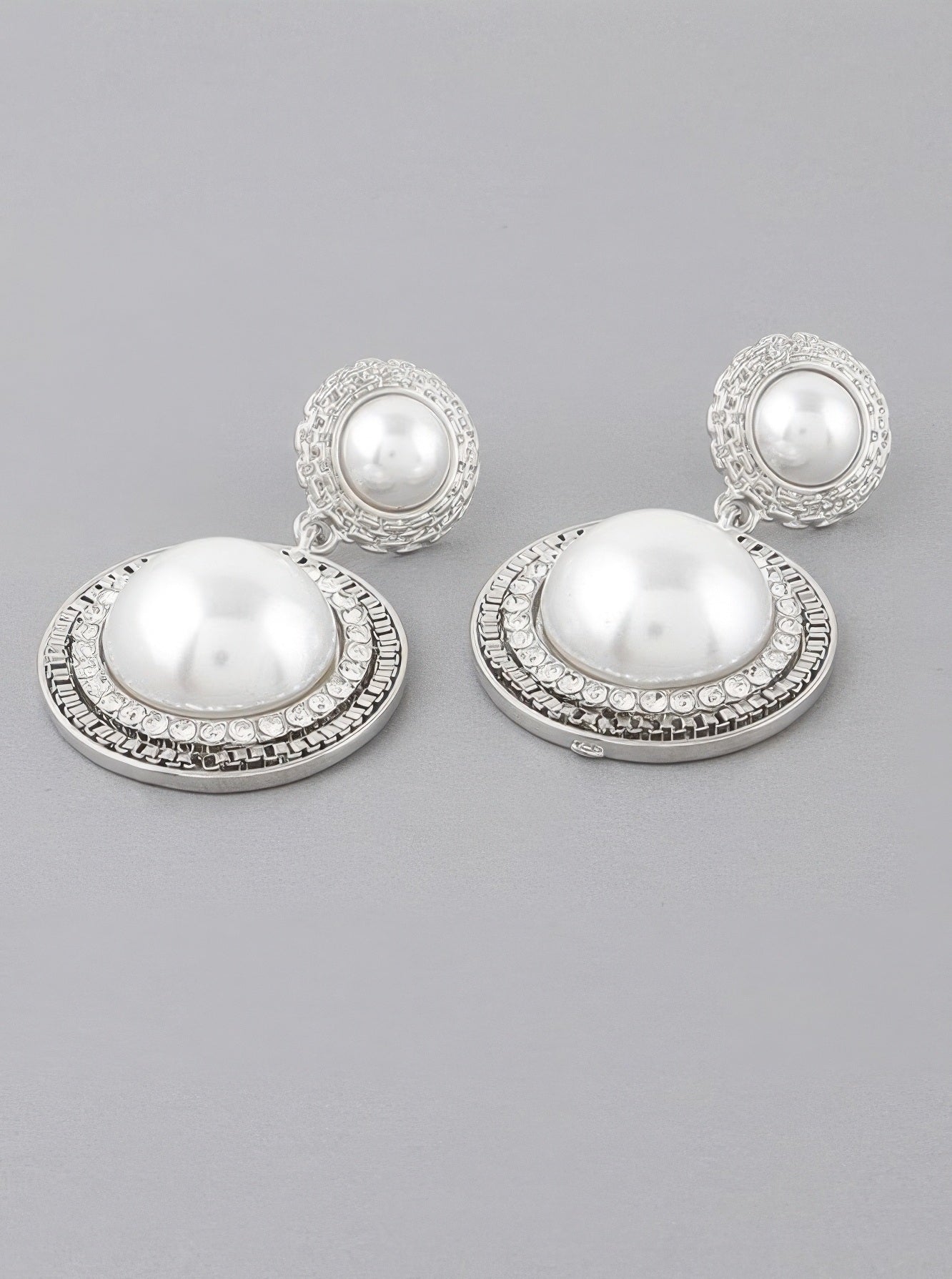 A pair of silver cream colored double framed pearl drop earrings.