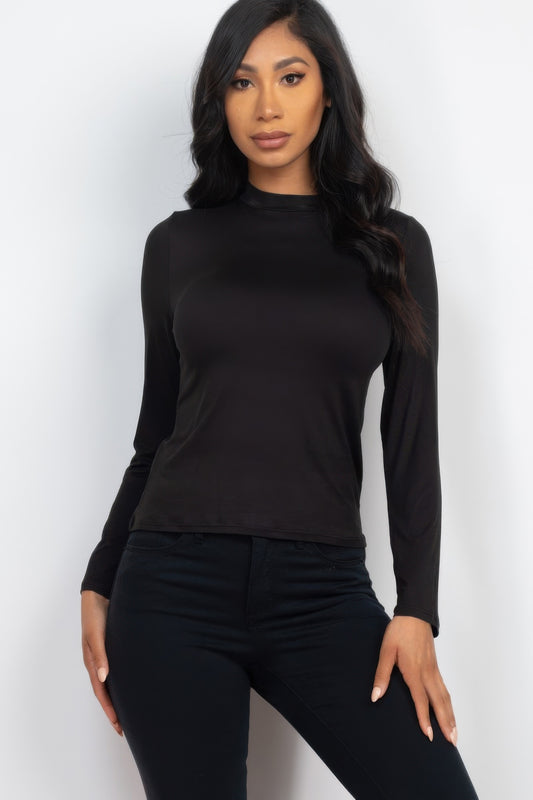 A woman posing in a black mock neck long sleeve top.
