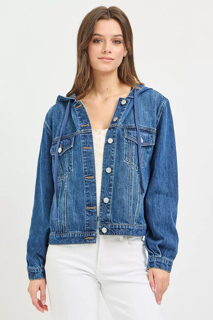 A woman posing in a medium wash denim jacket with hoodie.