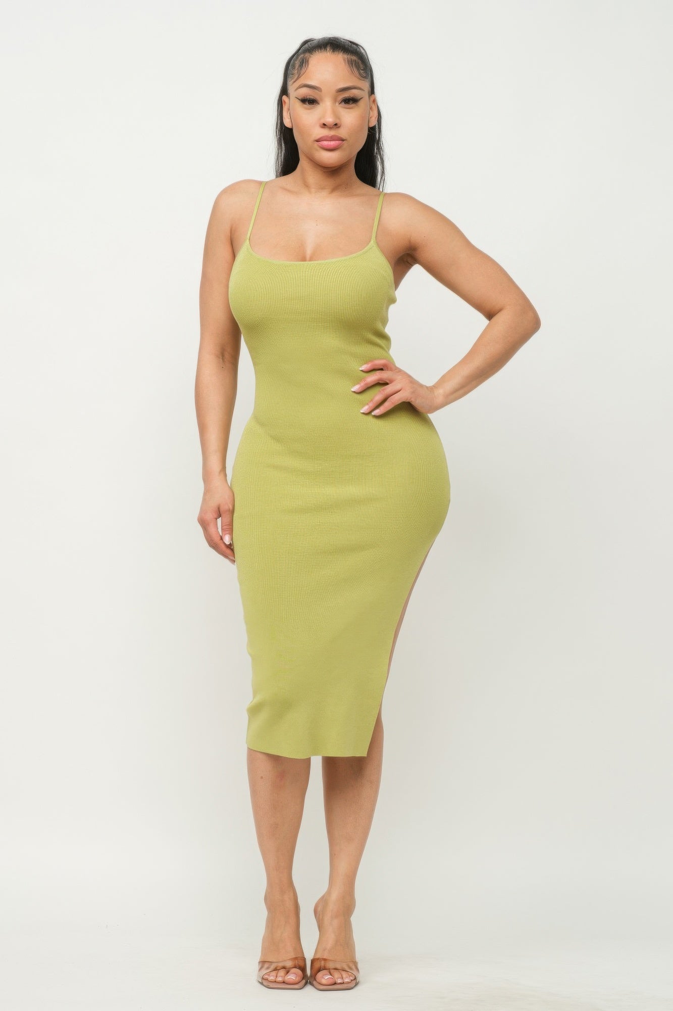 A woman posing in a green bean colored slit cami dress.