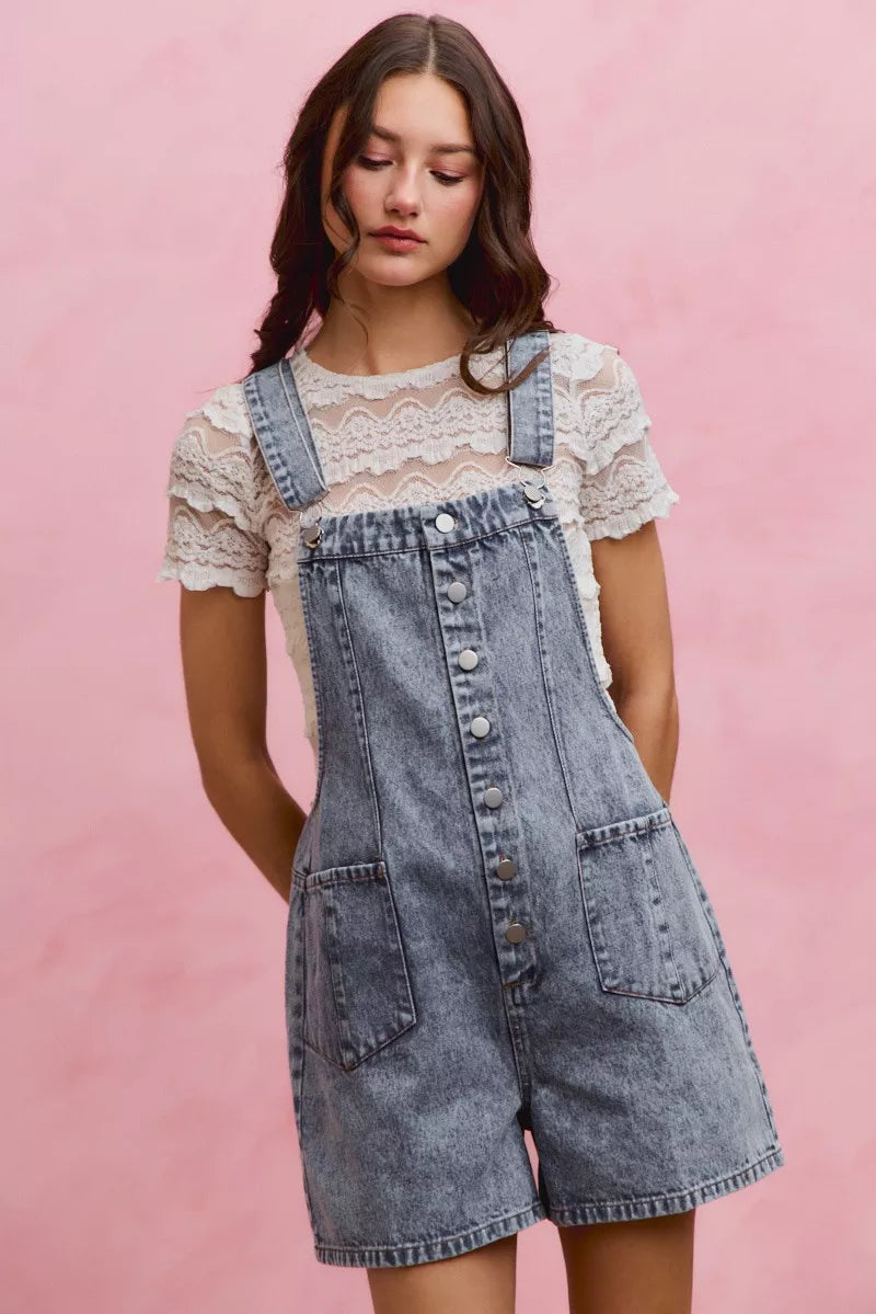 A woman posing in a light wash denim adjustable strap romper.