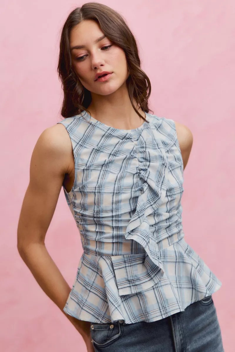 A woman posing in a blue plaid sleeveless ruffle peplum top.