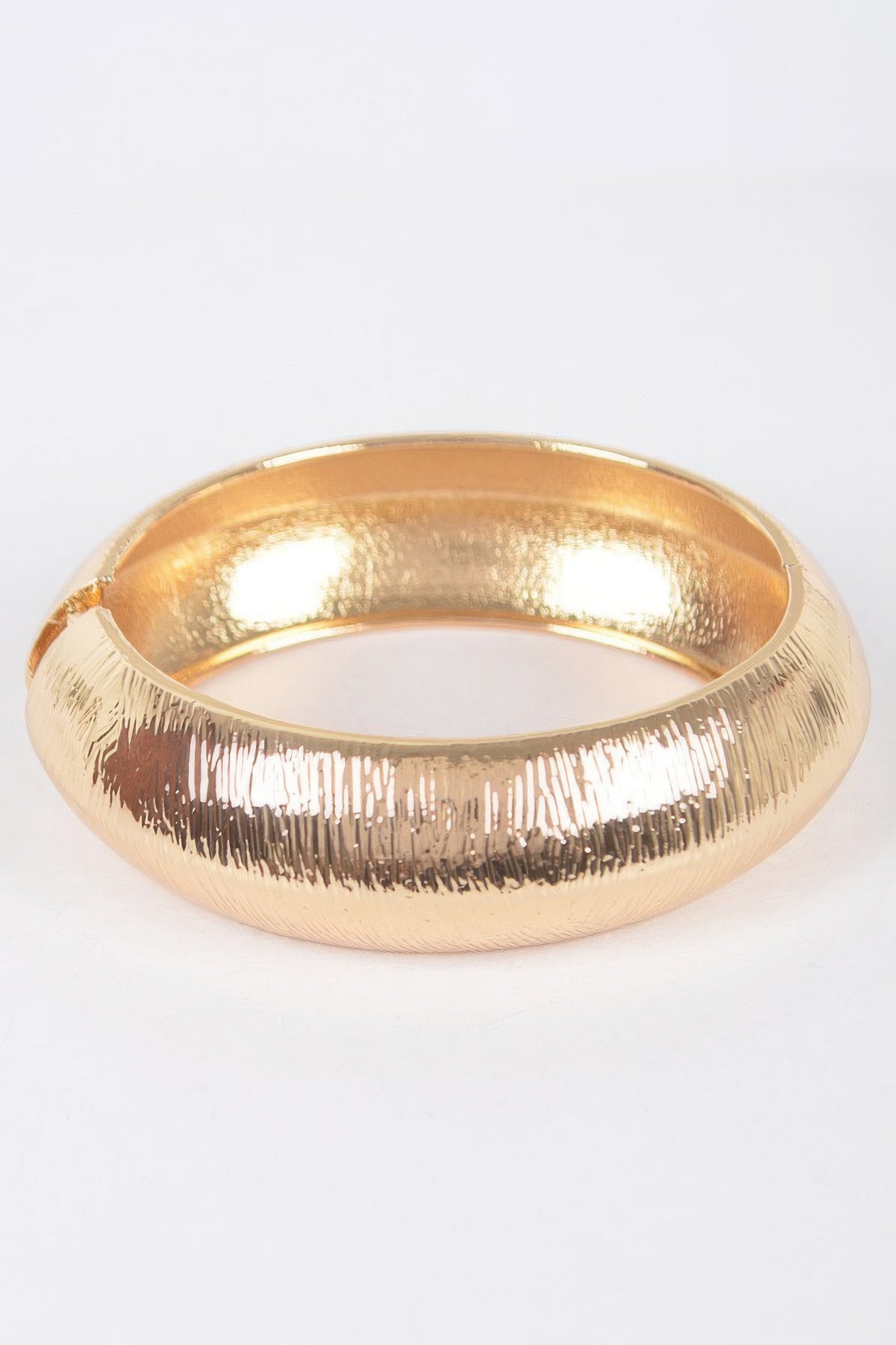 A gold textured metal bangle bracelet.