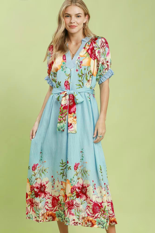 A woman posing in a blue floral border print midi dress.