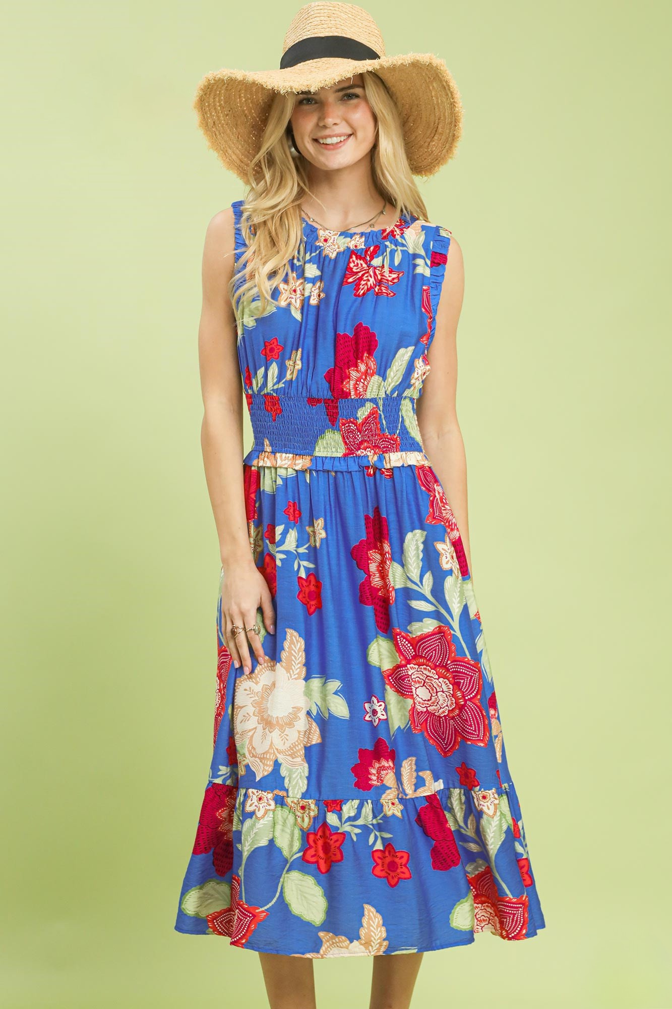 A woman posing in a blue floral smocked midi dress with a straw hat.