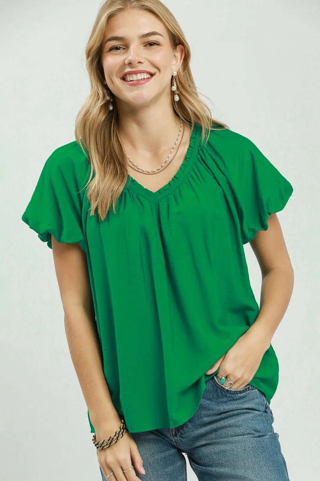 A woman posing in a green gathered v-neck top.