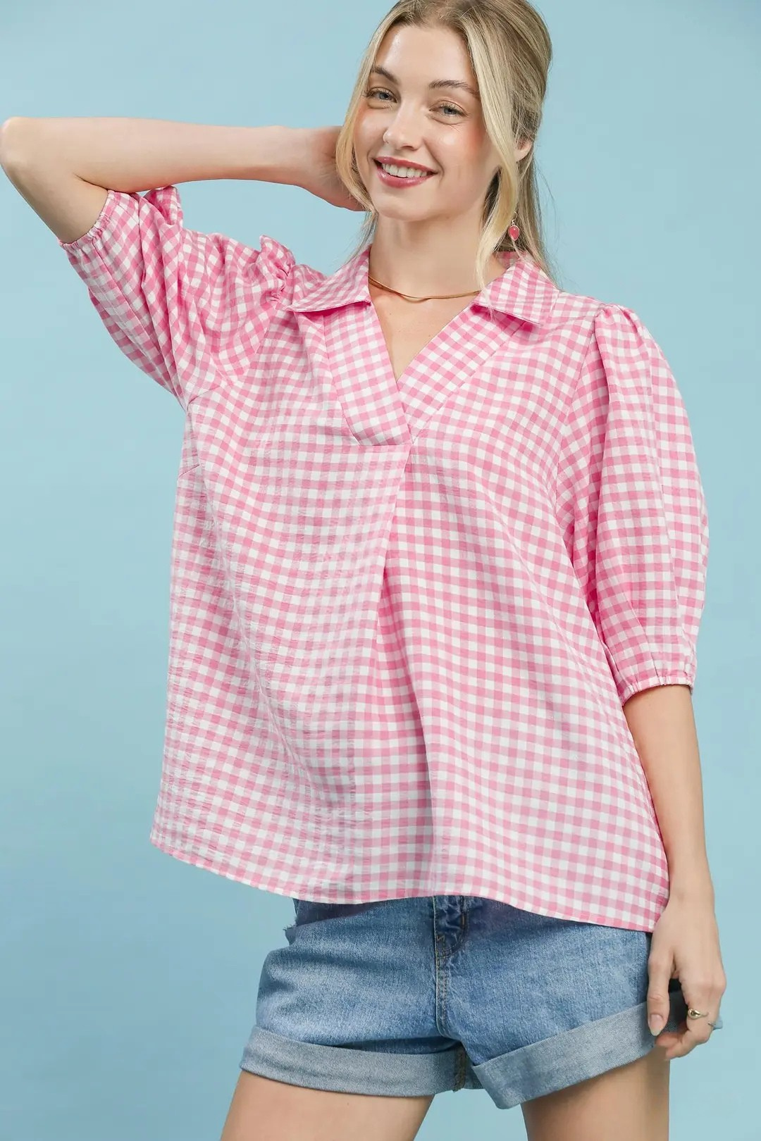 A woman posing in a peony pink gingham puff sleeve collar blouse.
