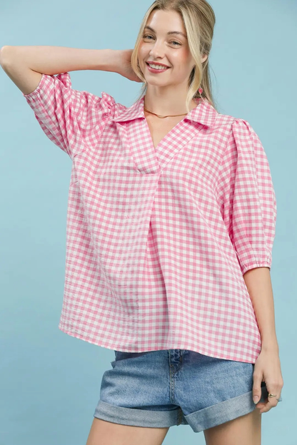 A woman posing in a peony pink gingham puff sleeve collar blouse.