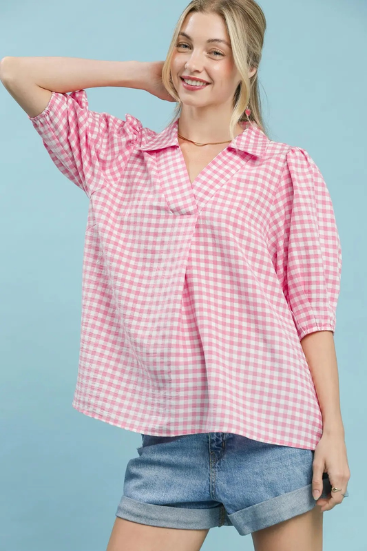 A woman posing in a peony pink gingham puff sleeve collar blouse.