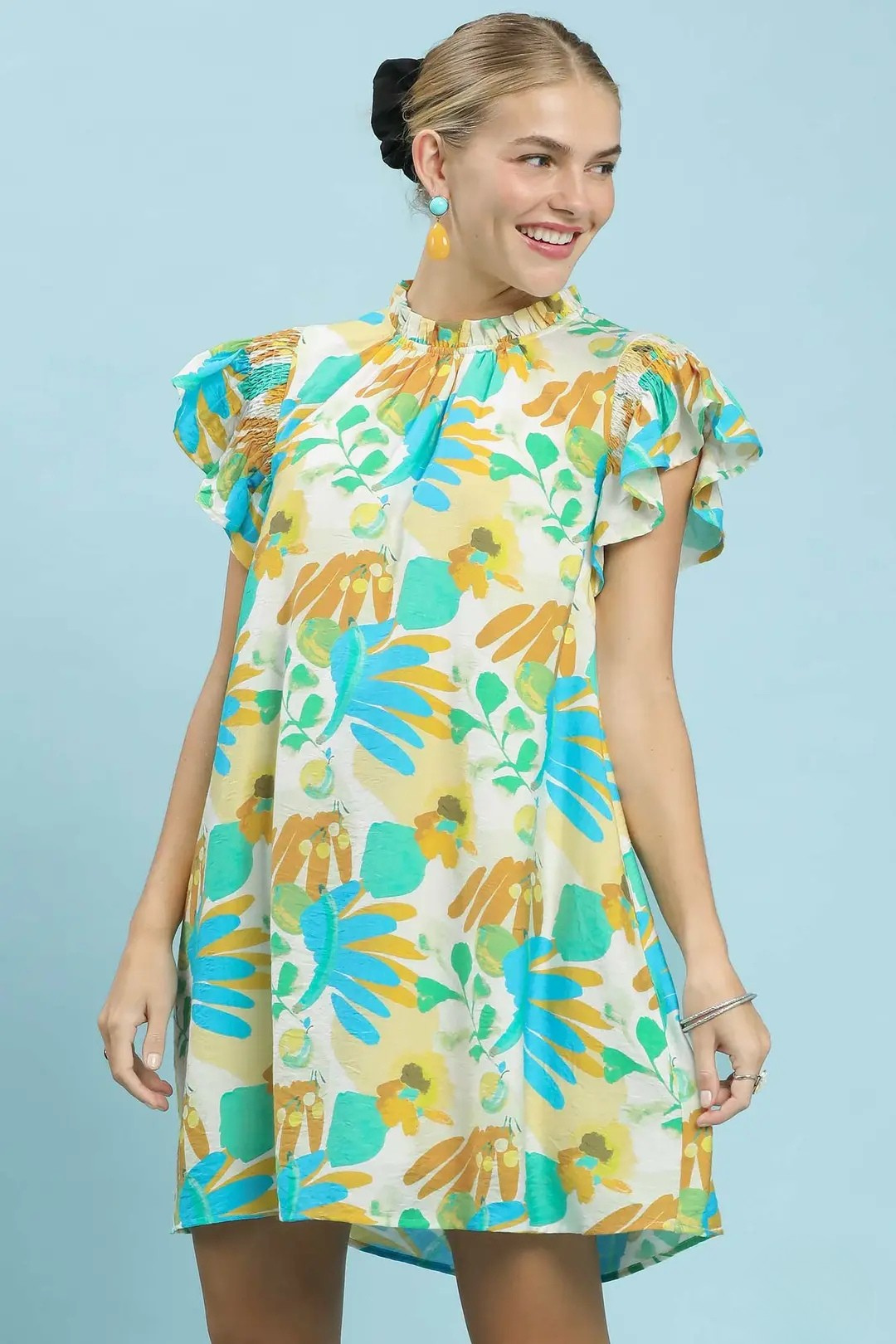 A woman posing in a jade ruffled botanical print mini dress.
