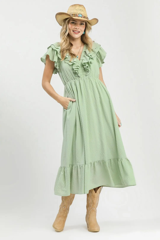 A woman posing in a sage colored ruffle midi dress with textured fabric.