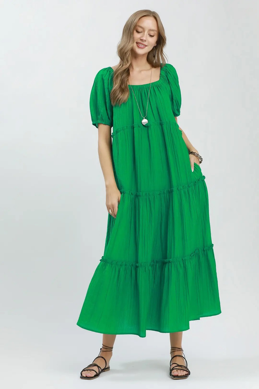 A woman posing in a green tiered midi textured dress.
