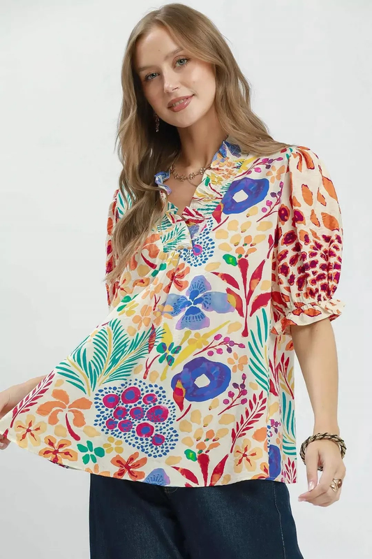 A woman wearing a colorful v-neck ruffle trim puff sleeve top with a floral design.