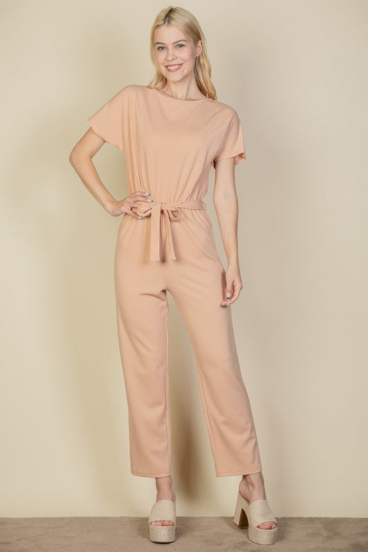 A woman posing in a khaki waist tie relaxed jumpsuit.